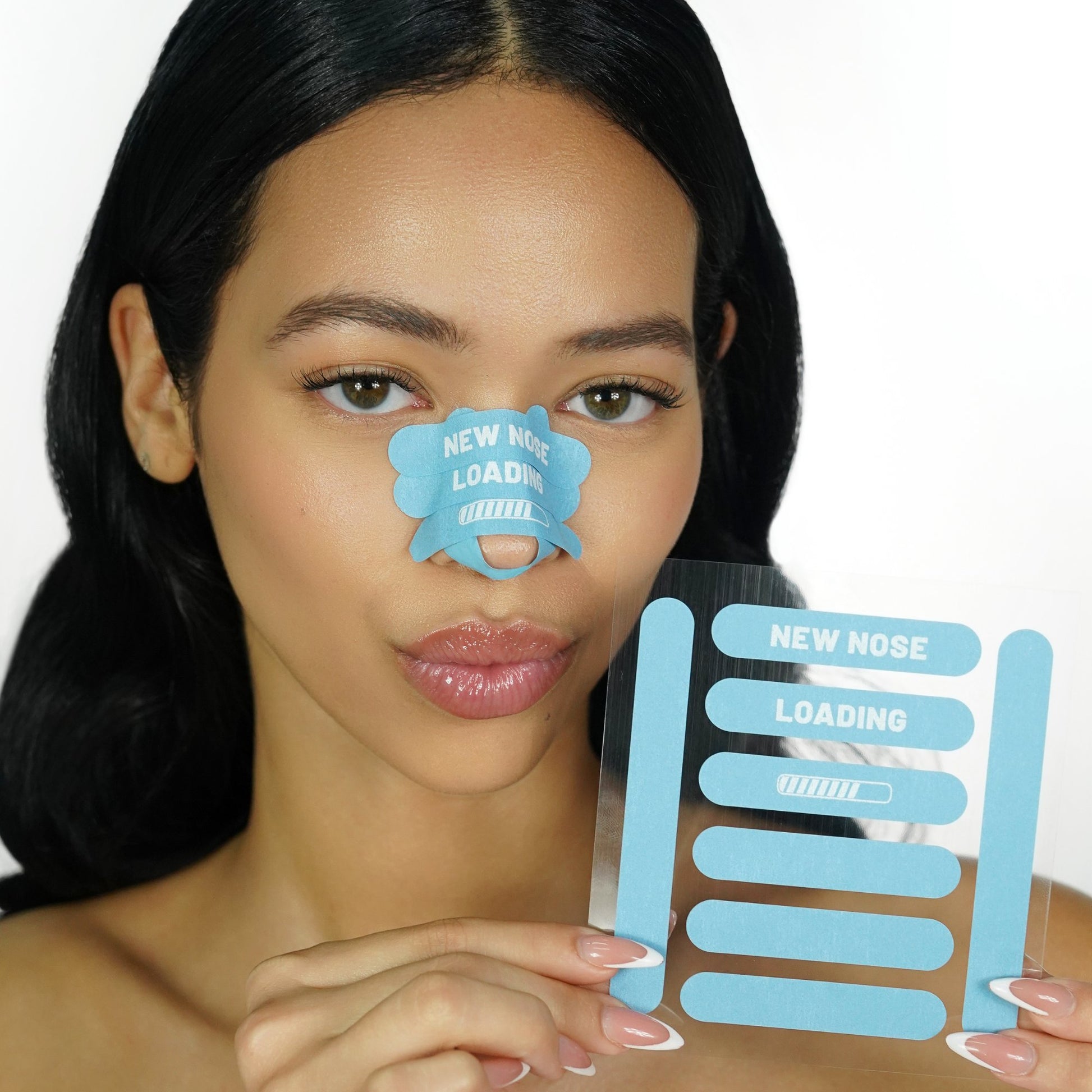 Woman holding a sheet of blue 'recovery babe' adhesive pre-cut nose strips with 'new nose loading' text, with matching strips on her nose, on a white background