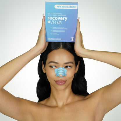 Woman holding blue 'recovery babe' product box over her head, with blue pre cut adhesive rhinoplasty nose strips, with 'new nose loading' text, on her nose.