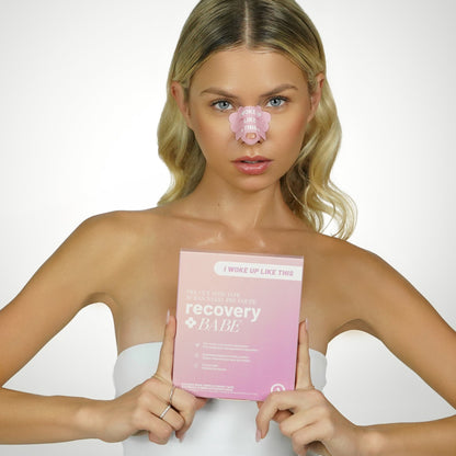 Woman with pink pre cut adhesive rhinoplasty nose strips, with 'I woke up like this' text, on her nose, holding a 'recovery BABE' product box.